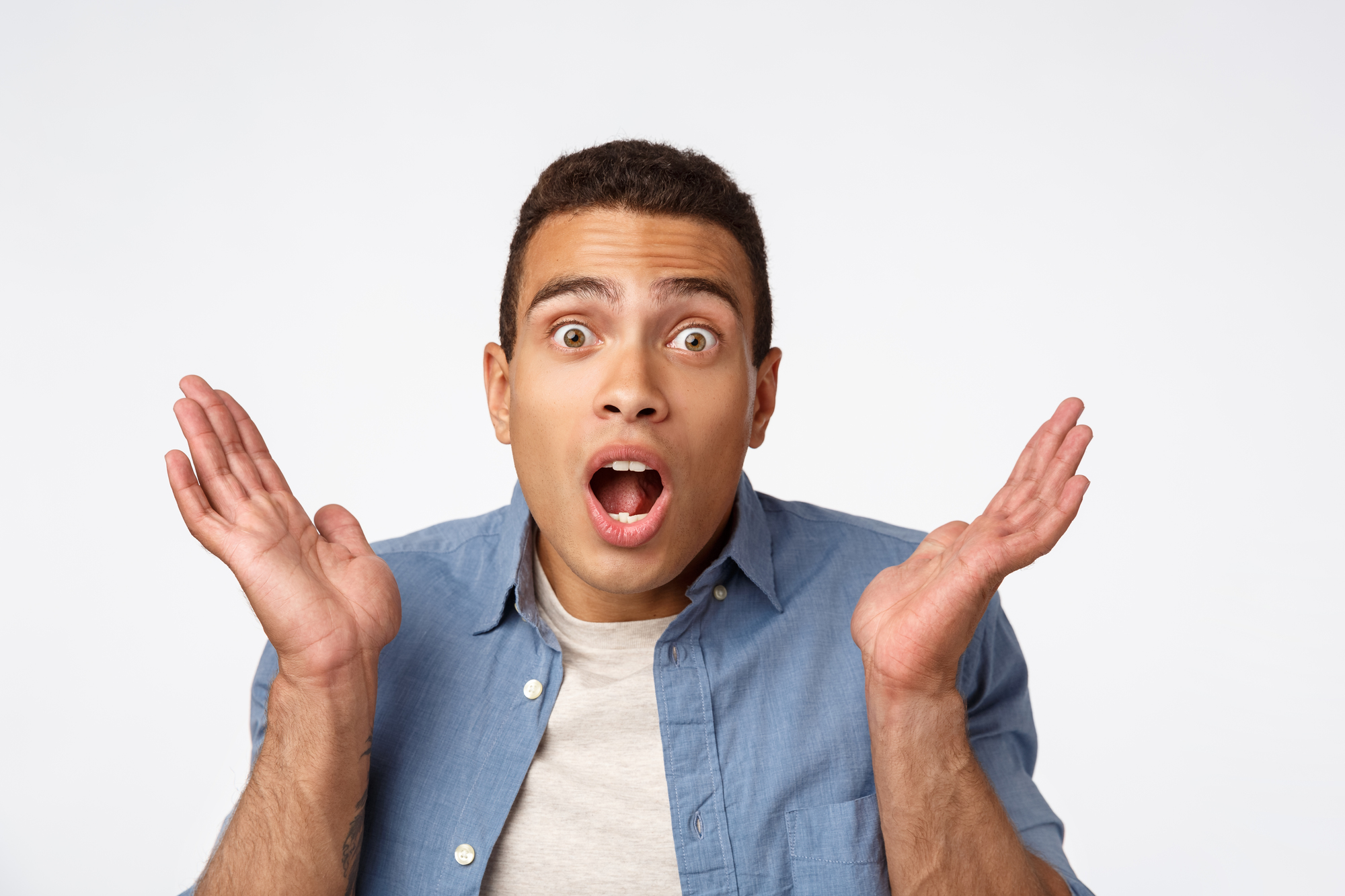 Close-up handsome masculine brazilian man in blue shirt over t-shirt, raising hands up stunned, open mouth, gasping fascinated popping eyes camera, hear surprising amazing news, white background